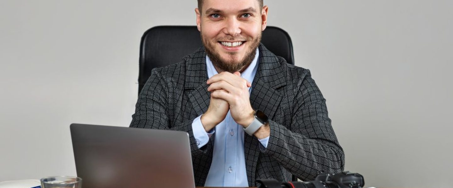 bearded male photographer smiling while working at her desk.