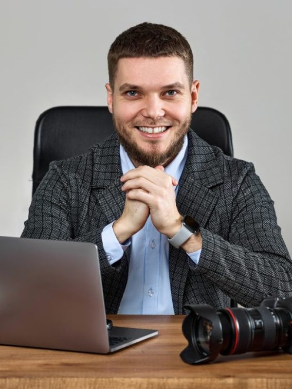 bearded male photographer smiling while working at her desk.